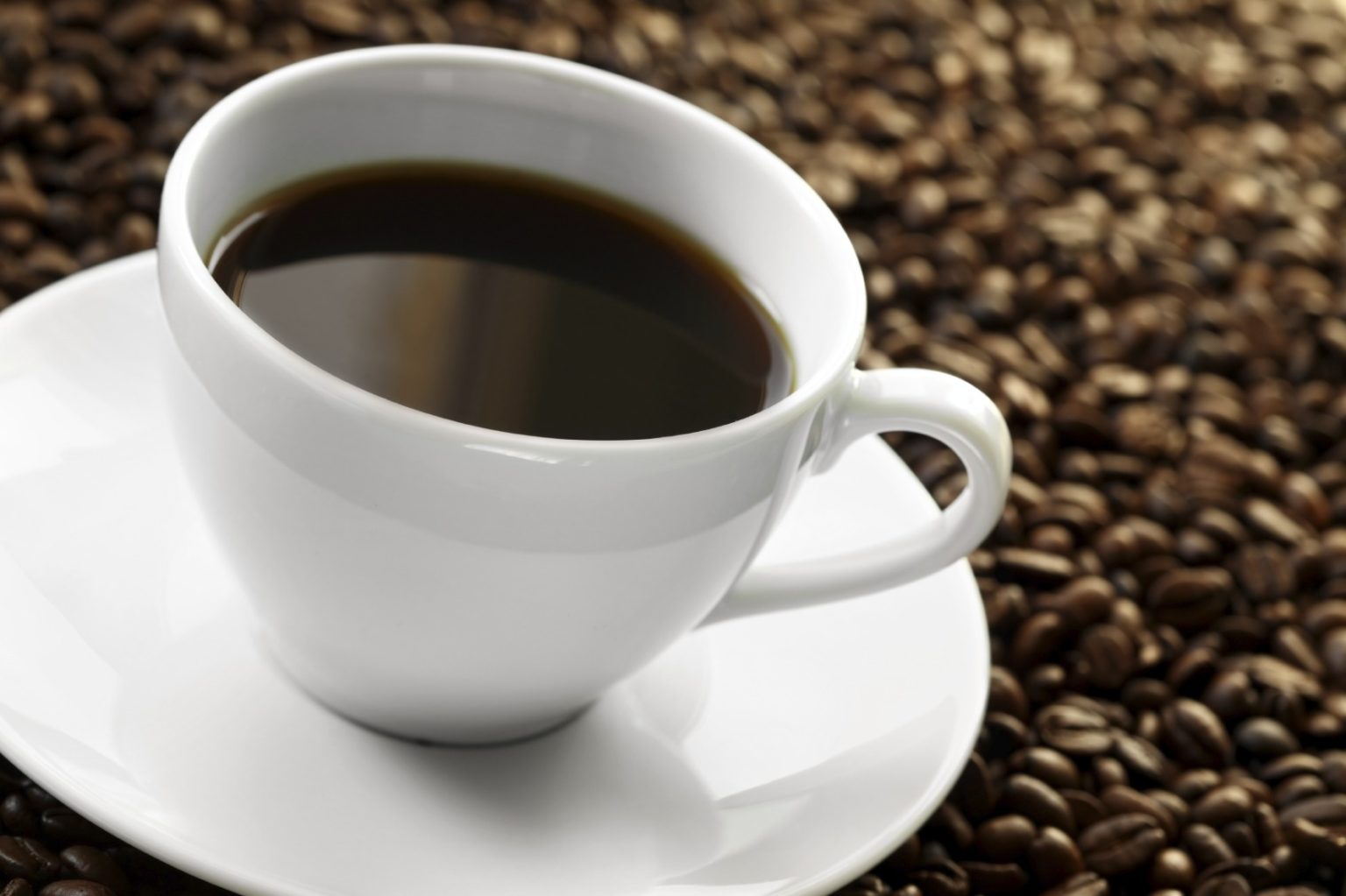En kopp kaffe på ett fat med kaffebönor i bakgrunden